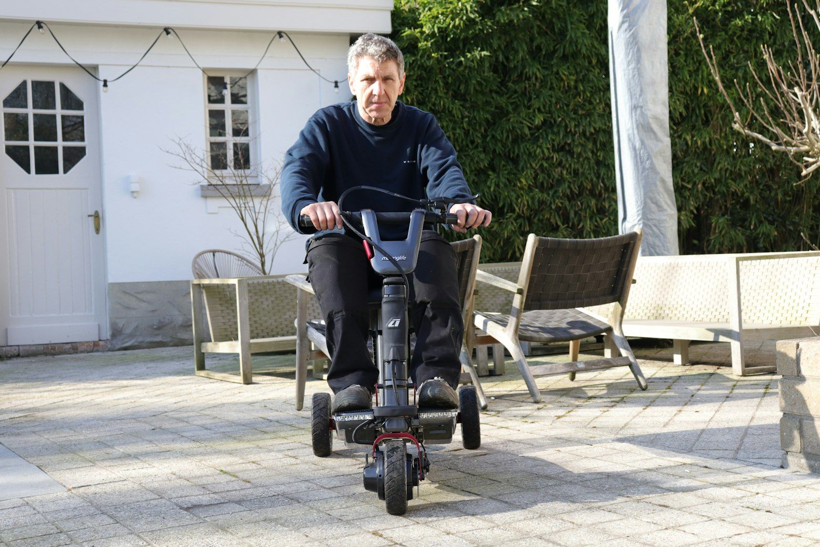 A man riding a compact mobility scooter across a paved courtyard